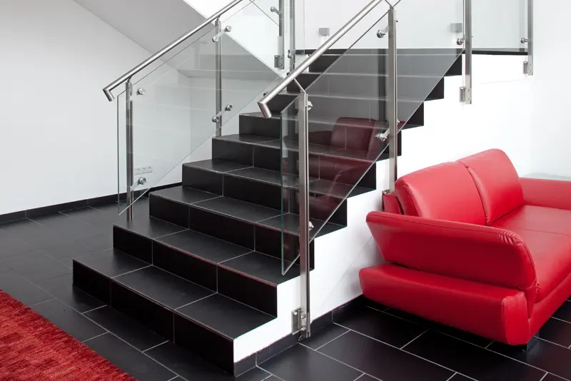 Moderner Eingangsbereich mit schwarzer Treppe und Glasgeländer, daneben eine rote Ledercouch und schwarzer Fliesenboden.