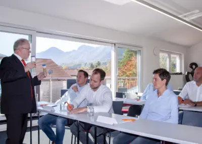 Rüdiger Krethe explains a lubricant topic using samples to attentive participants in a room with a mountain view.