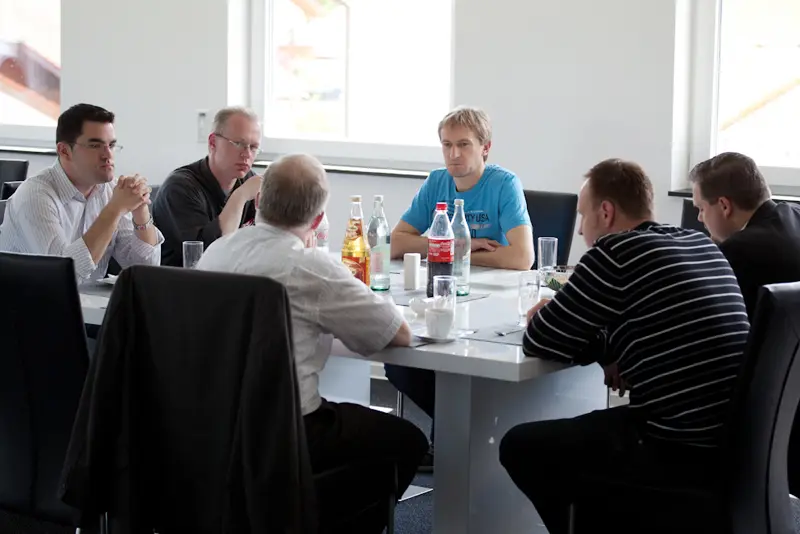 Gruppe von Seminarteilnehmern sitzt an einem Tisch im Pausenraum, spricht miteinander und hat Getränke und Tassen vor sich stehen.