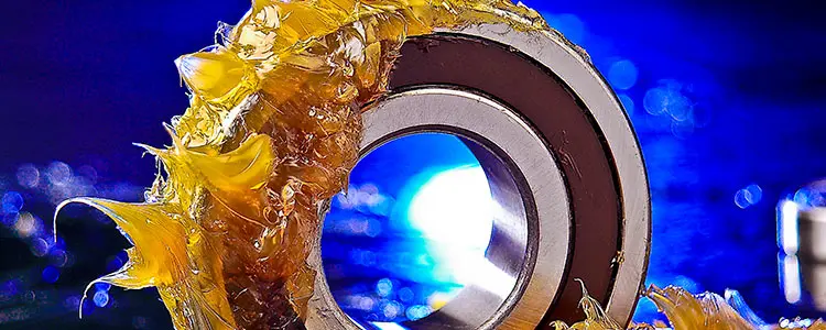Metal ball bearing, generously coated with yellow grease, against a blue background