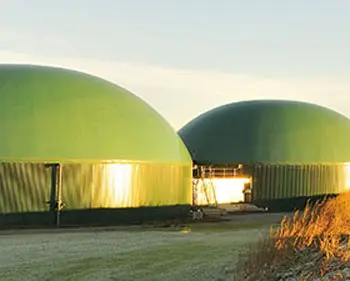 Two green fermenter domes of a biogas plant in a rural setting at sunrise
