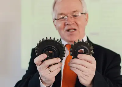 Rüdiger Krethe holds two gears in his hands and explains the differences and possible wear and tear.