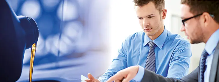 Two experts discussing documents; on the left, engine oil is being poured from a canister – symbolizing a seminar on the basics of lubrication.
