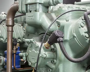 Several green industrial compressors with piping and attachments in a plant hall