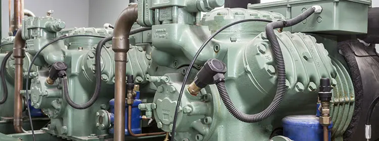 Lubricating compressors correctly – Compressor oil for reliable industrial equipment Several green industrial compressors with piping and attachments in a plant hall