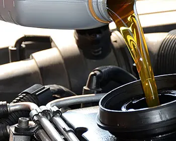 Golden motor oil is poured from a canister into a car engine.